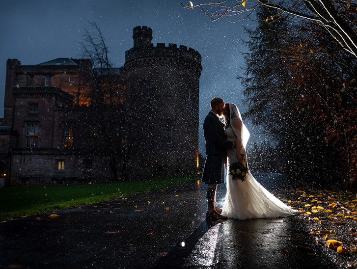 Bride and groom evening kiss in the rain with the shadow of Dalhousie Castle in background